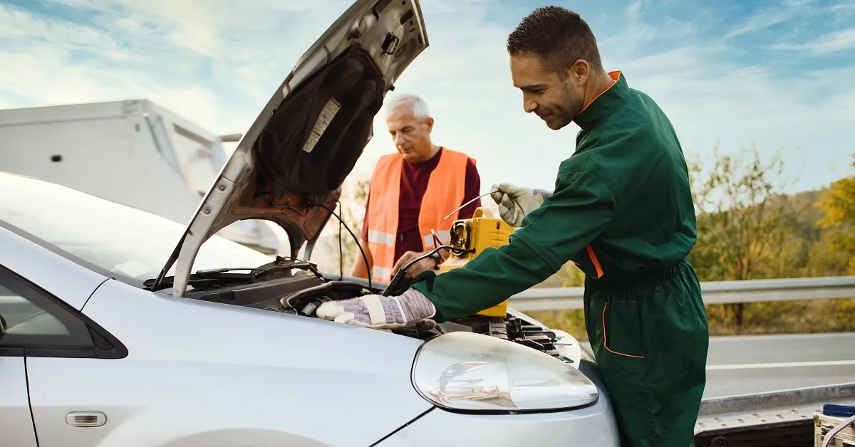 Two road assistant workers in towing service trying to start car engine with jump starter and energy station with air compressor. Roadside assistance concept.